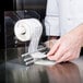 A hand using a Noble Products Plexiglas Label / Sticker Dispenser to hold a roll of food labels.