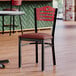 A Lancaster Table & Seating side chair with a burgundy vinyl seat and mahogany wood back on a table in a restaurant.