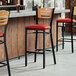 A row of Lancaster Table & Seating bar stools with red vinyl seats and natural wood backs.