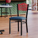 A Lancaster Table & Seating black side chair with a navy vinyl seat and mahogany wood back on a table in a restaurant dining area.