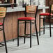 A Lancaster Table & Seating bar stool with a red vinyl seat and natural wood back.