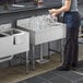 A woman standing at a Regency stainless steel underbar drainboard with glasses on it.
