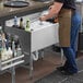 A woman in an apron pouring liquid into a Regency underbar ice bin with bottle holders.