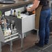 A woman making a drink at a stainless steel underbar ice bin with bottle holders.