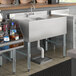 A Regency underbar sink with a counter top and bottles of liquor on a shelf.