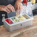 A man using an American Metalcraft stainless steel condiment bar to put a lemon slice into a container of fruit.