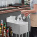 A woman standing in front of a stainless steel underbar drainboard holding glasses.