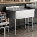 A stainless steel underbar drainboard with a grated surface and four legs, designed for commercial bar use.