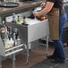 A woman in a brown apron pouring ice into a Regency underbar ice bin with bottle holders.