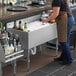 A woman wearing an apron pours a drink into a glass from a Regency underbar ice bin with bottle holders.