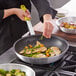 A person using a Choice yellow silicone pan handle sleeve to cook food in a pan.