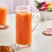 An Acopa slim glass pitcher of orange juice with lemon slices next to a glass of orange juice.