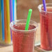 A clear plastic cup filled with a red beverage and a green neon smoothie straw.