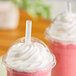 A translucent, pointed, unwrapped smoothie straw inserted into a pink smoothie with whipped cream in a clear plastic cup.
