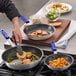 A person cooking potatoes and sausage in a Choice aluminum frying pan.