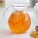 An Acopa Fishbowl glass pitcher of orange juice on a table.