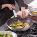 A person cooking food in a pan using a Choice black silicone pan handle sleeve.