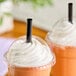 A black pointed unwrapped straw inserted into a plastic cup with a dome lid and whipped cream topping.