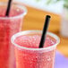 A black pointed unwrapped smoothie straw placed in a clear plastic cup filled with a red slushy beverage.