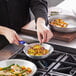 A person cooking meat and vegetables in a Choice aluminum fry pan.
