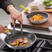A person using a yellow Choice silicone handle sleeve on a pan to cook sausages and potatoes.