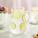 An Acopa round glass pitcher of water with lemon and lime slices and ice.