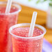 A clear plastic cup filled with a red iced beverage and a translucent pointed smoothie straw.