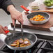 A person using red Choice silicone pan handle sleeves on a pan of sausages and potatoes.