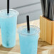 A couple of blue drinks in plastic cups with black straws.