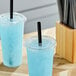 Two blue drinks in plastic cups with black pointed straws on a table.