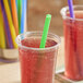A clear plastic cup filled with a red beverage and a green neon pointed straw, with other colorful straws visible in the background.
