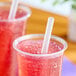 A clear plastic cup filled with a red beverage and a translucent pointed unwrapped smoothie straw.