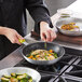 A person cooking food in a Choice aluminum non-stick fry pan.