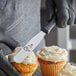 A person in black gloves using a Mercer baking spatula to frost cupcakes.