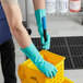A person in green Cordova nitrile gloves holding a yellow container.