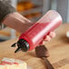A hand holding a OXO clear plastic squeeze bottle with red liquid being poured into a sandwich.
