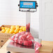A stainless steel AvaWeigh tower on a counter with a bag of oranges on the scale.