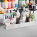 A person holding a green Regency double tier speed rail with bottles on a bar counter.