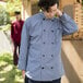 A man in a long Uncommon Chef coat looking at something on a counter in a professional kitchen.