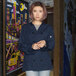 A woman wearing an Uncommon Chef long sleeve chef coat with 10 buttons in a professional kitchen.