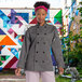 A woman in a grey Uncommon Chef long sleeve chef coat standing in a professional kitchen.