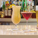 A group of Front of the House Tritan plastic hurricane glasses filled with pink drinks on a bar.