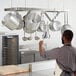 A man in a kitchen with metal pots hanging from a Regency stainless steel ceiling-mounted pot rack.