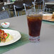 A Front of the House Drinkwise highball glass filled with cola next to a plate of food on a table.