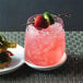 A Front of the House Drinkwise stemless wine glass with a drink and a strawberry and lime in it on a table.