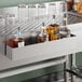 A 24-inch stainless steel single tier speed rail mounted to a bar for holding liquor bottles.