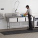 A man washing a Regency stainless steel three compartment sink.