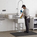 A man washing a Regency stainless steel commercial sink with 2 drainboards.