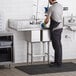 A man in a black shirt and grey pants cleaning a Regency stainless steel two compartment sink.