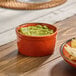 A small orange stoneware ramekin filled with guacamole.
